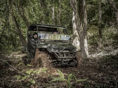 Two people riding in a 2019 Mahindra Retriever 1000 Gas Flexhauler Le through some mud in a …